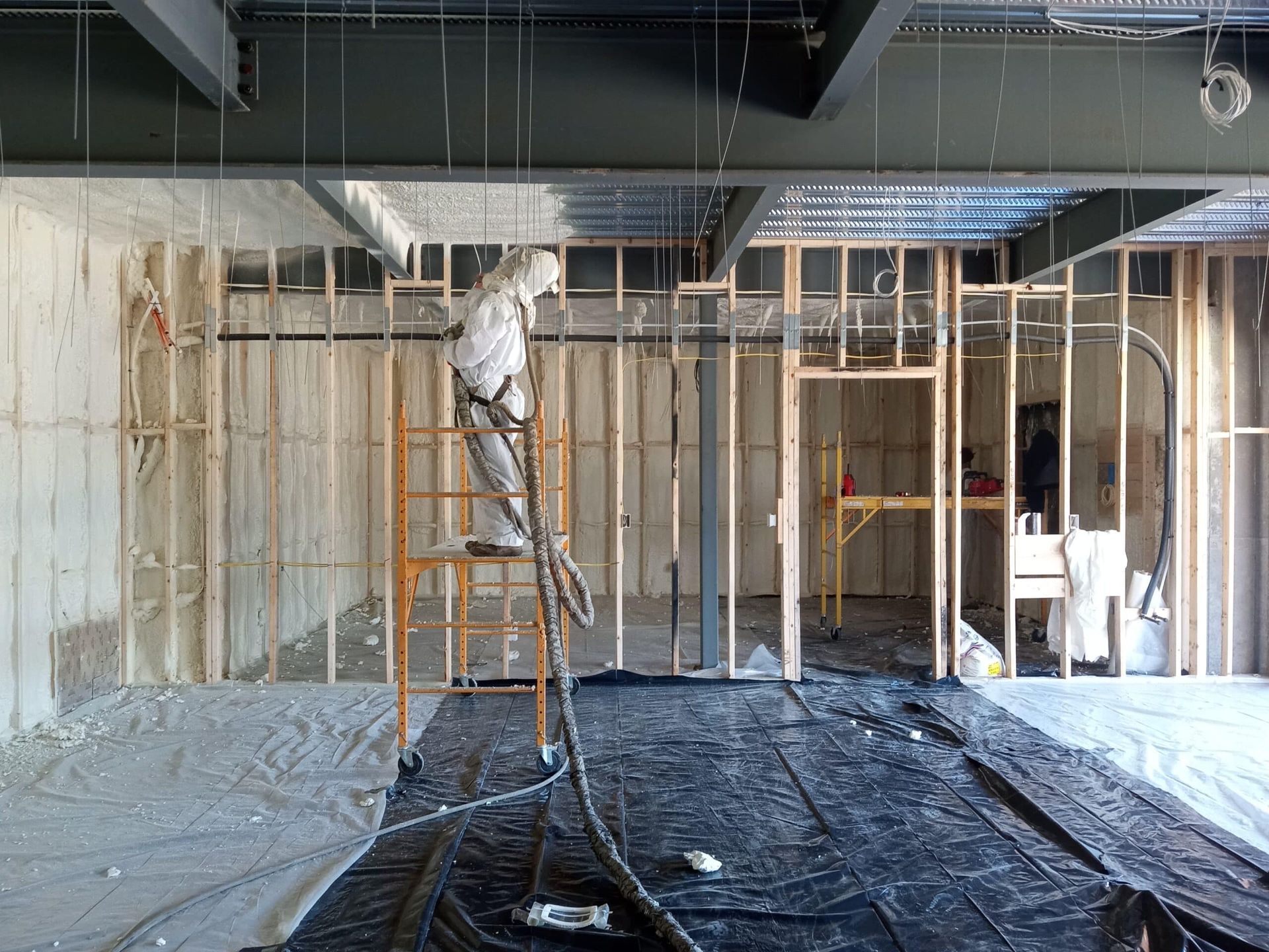 A man is spraying insulation on the ceiling of a building under construction.