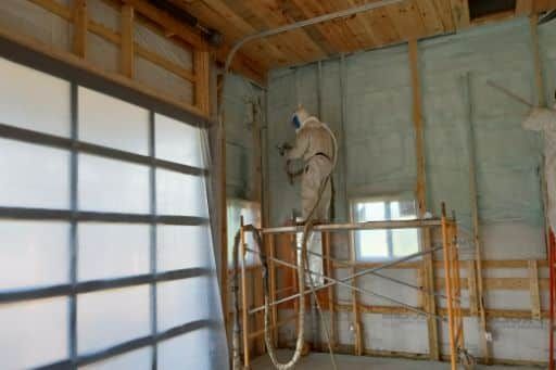 A man is spraying insulation on the walls of a garage.