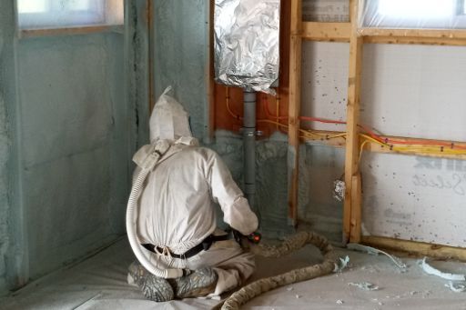 A man in a protective suit is spraying insulation in a room.