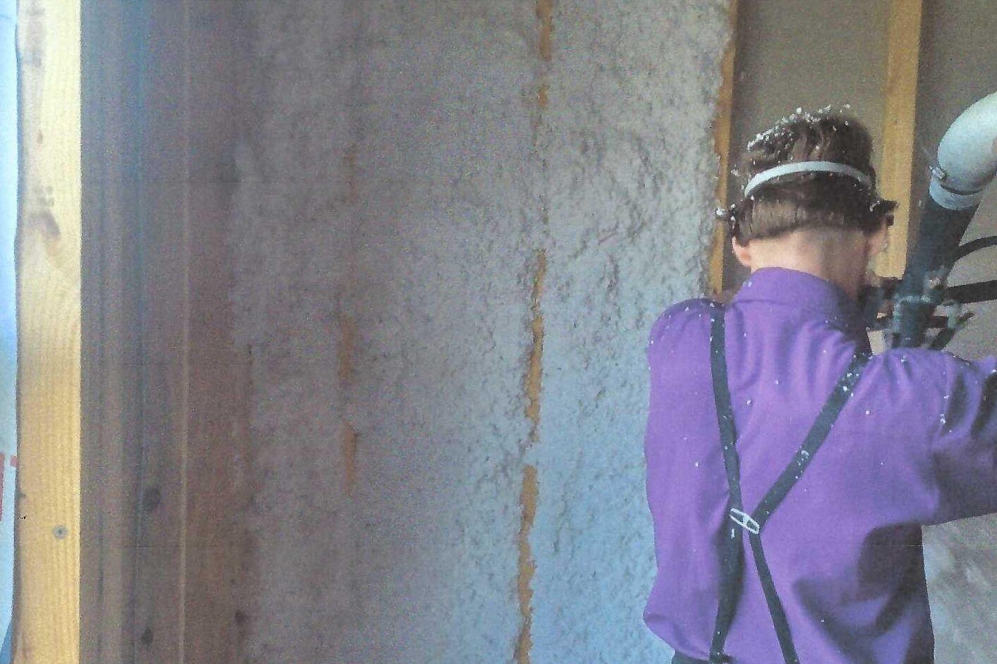 A man in a purple shirt is standing in front of a wall.