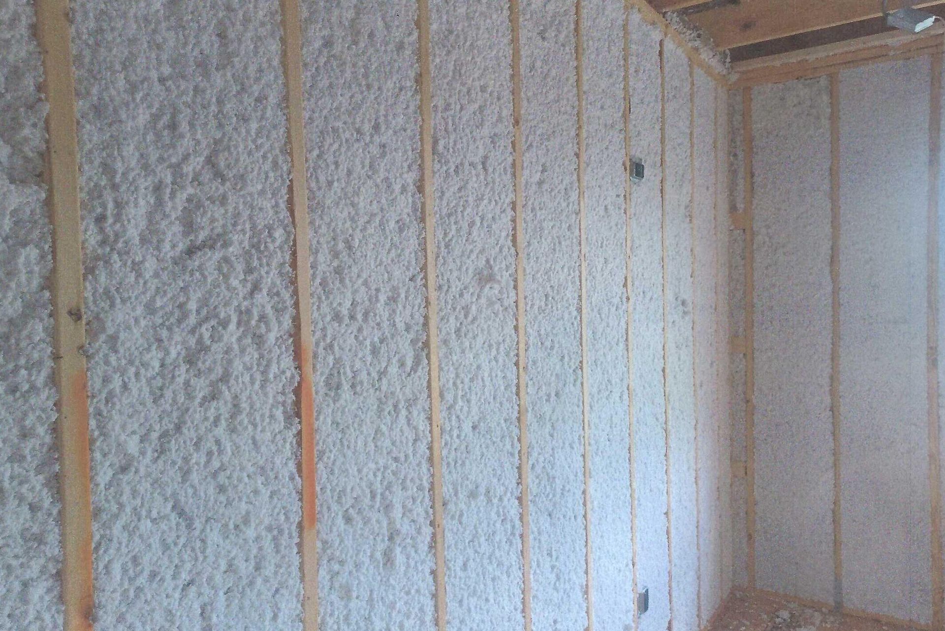 A room with white insulation on the walls and wooden beams.