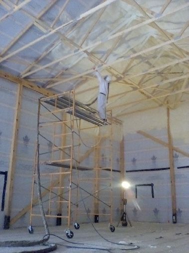 A man is spraying foam on the ceiling of a building.