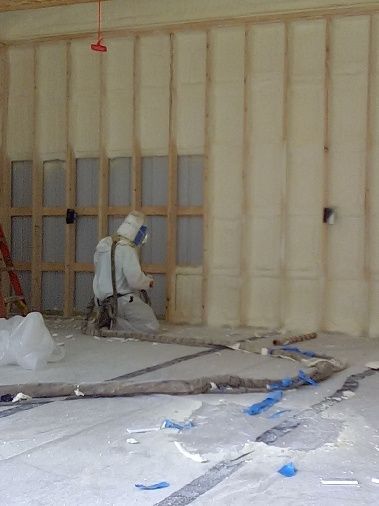 A man is spraying insulation on a wall in a room.
