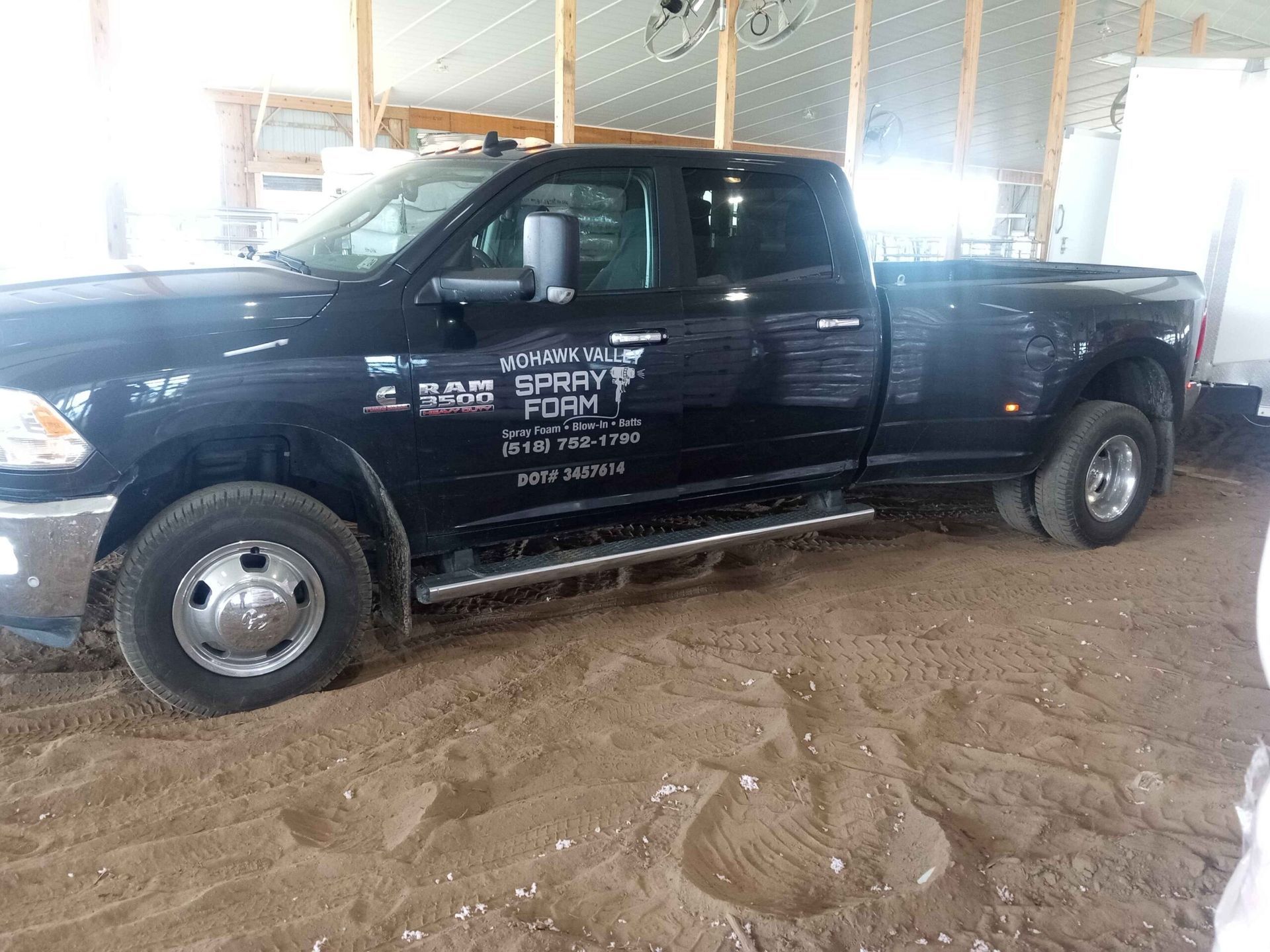 A black truck is parked in the dirt in a barn.