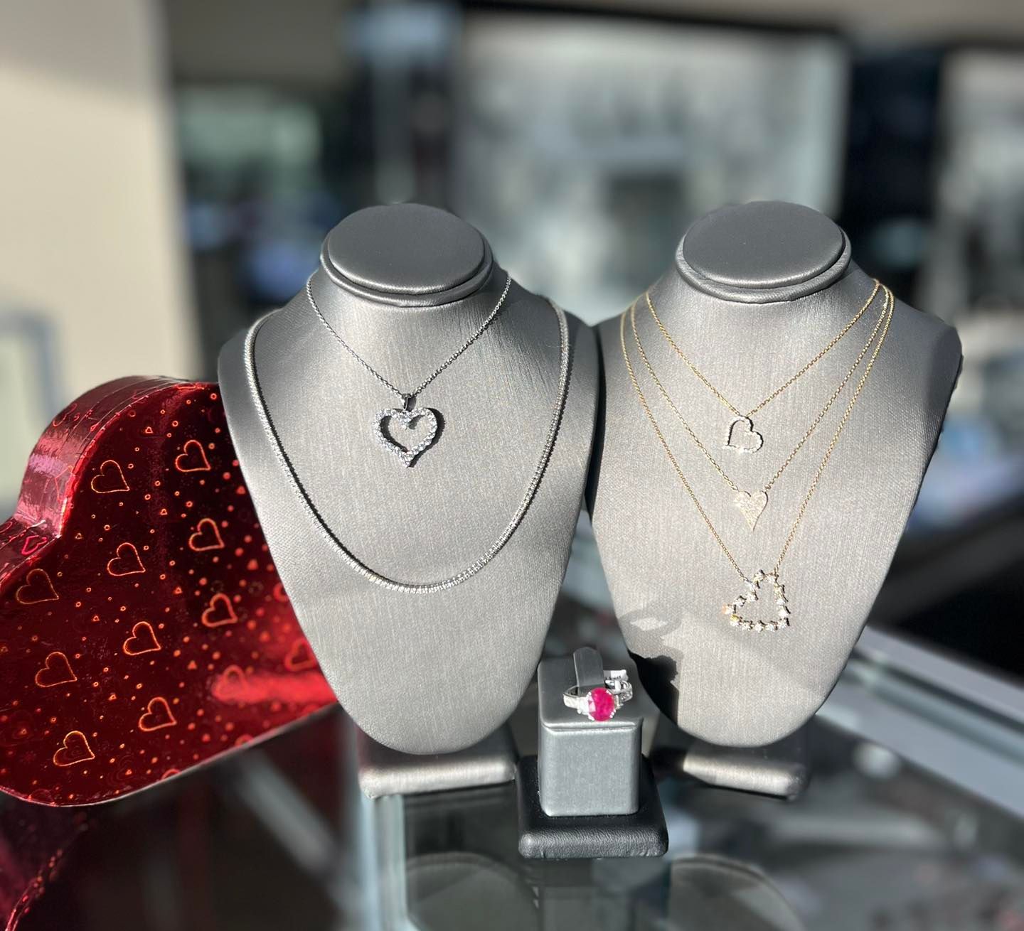 Jewelry display: necklaces with heart pendants on mannequins, a red heart box, and a ring.