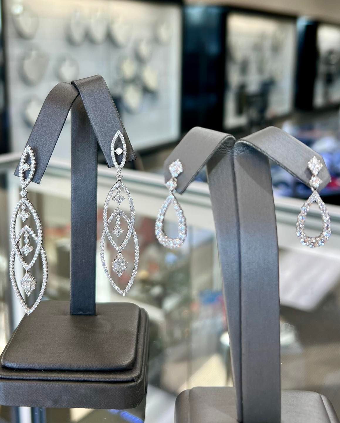 Two pairs of diamond earrings on display stands inside a jewelry store.