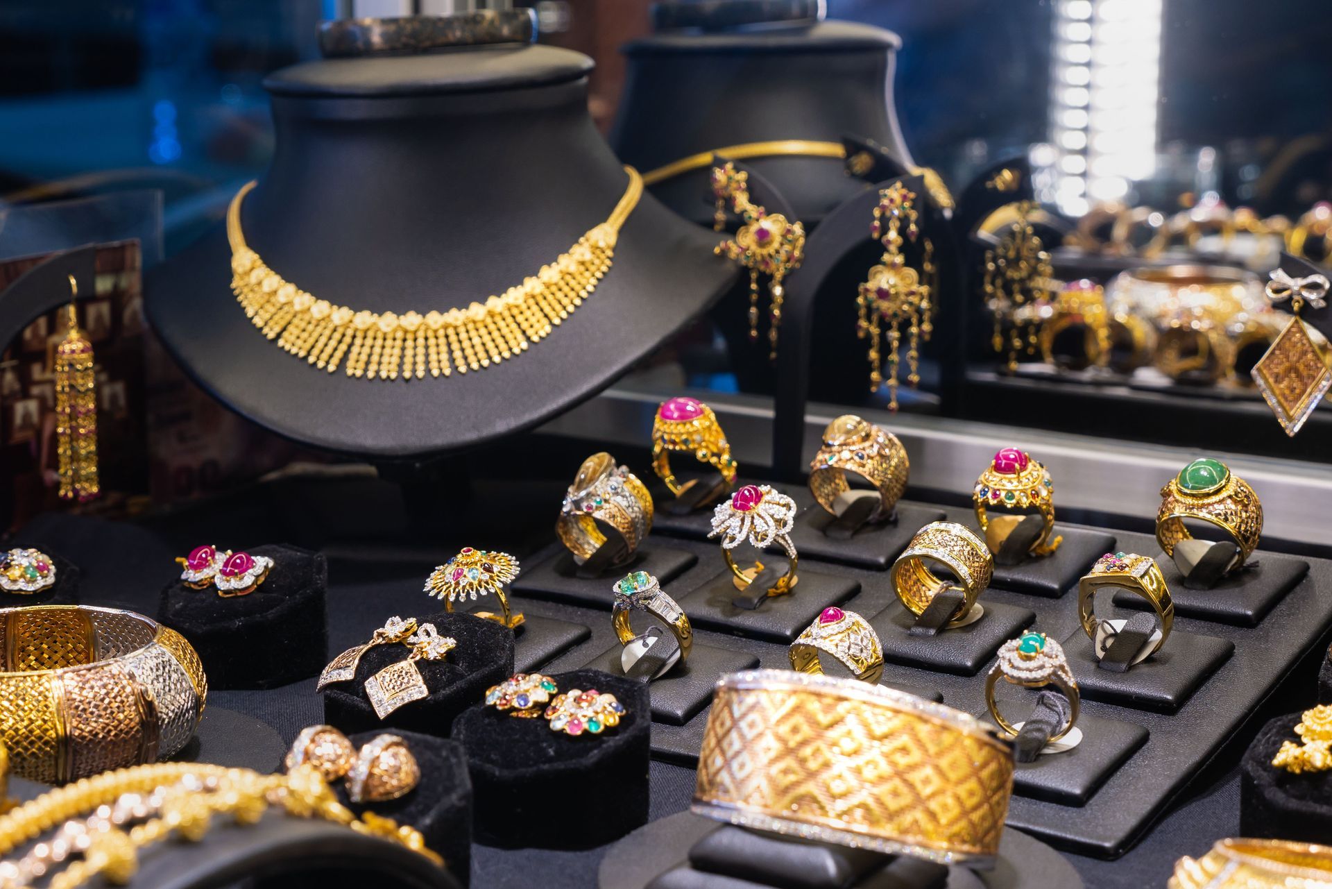 Jewelry display with gold necklaces, rings, and bracelets on black stands against a blurred backdrop.