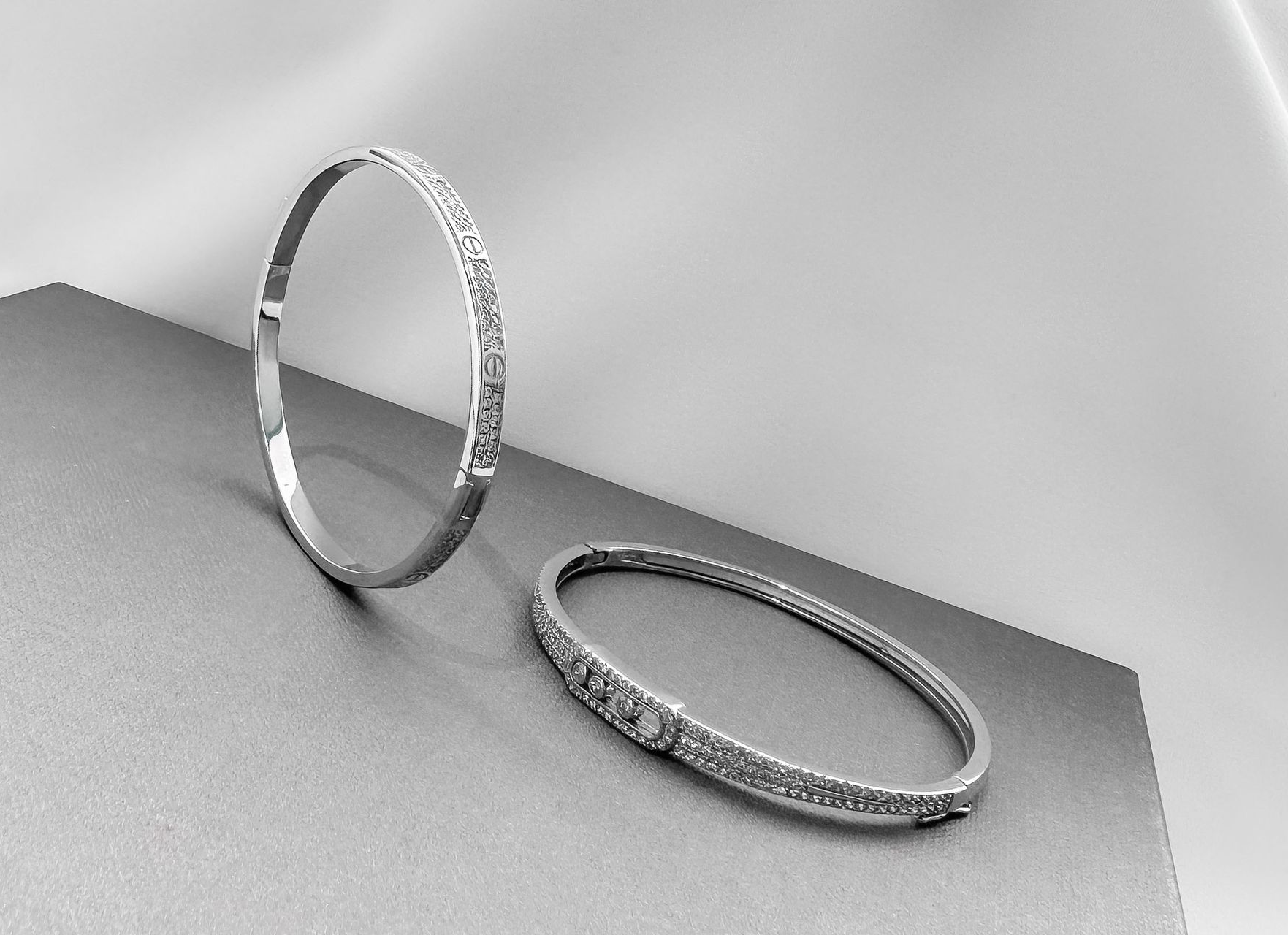 Two silver bracelets with embedded stones on a gray surface, with a white backdrop.