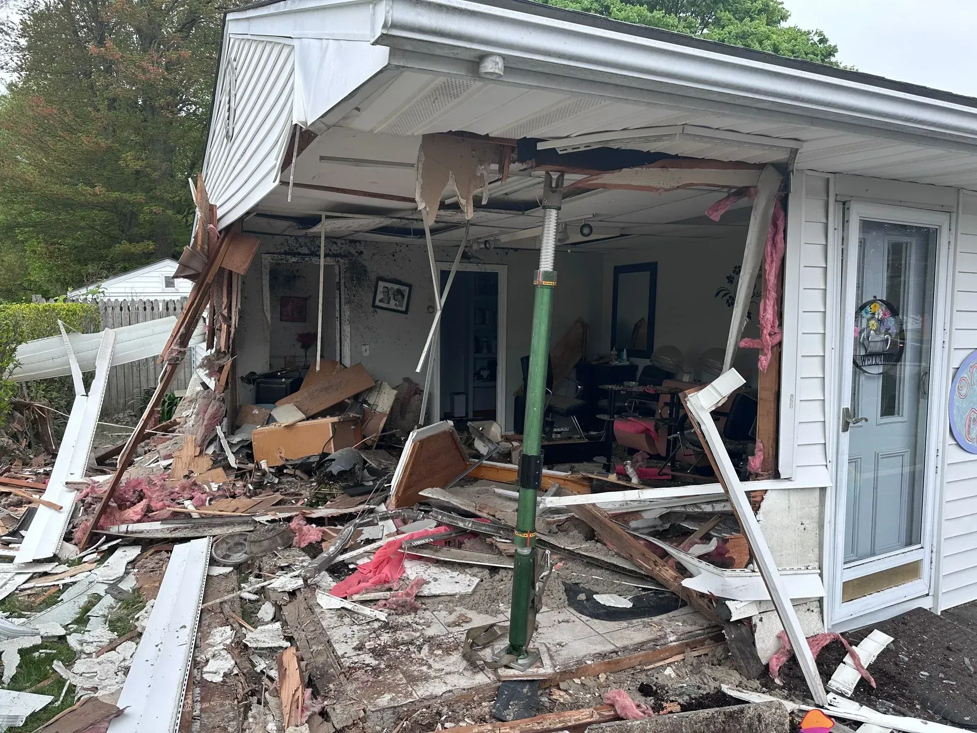 Damaged house front after a collision. Debris, exposed interior, temporary support beam.