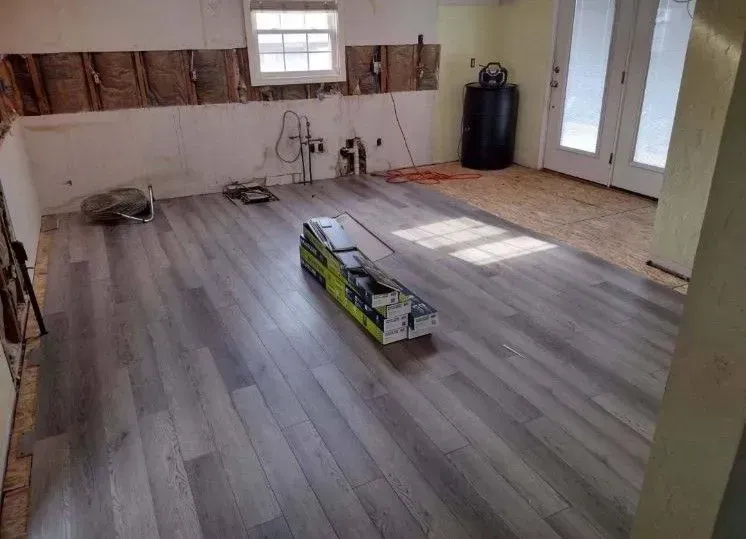 Room undergoing renovation, with gray laminate flooring laid and unfinished walls.