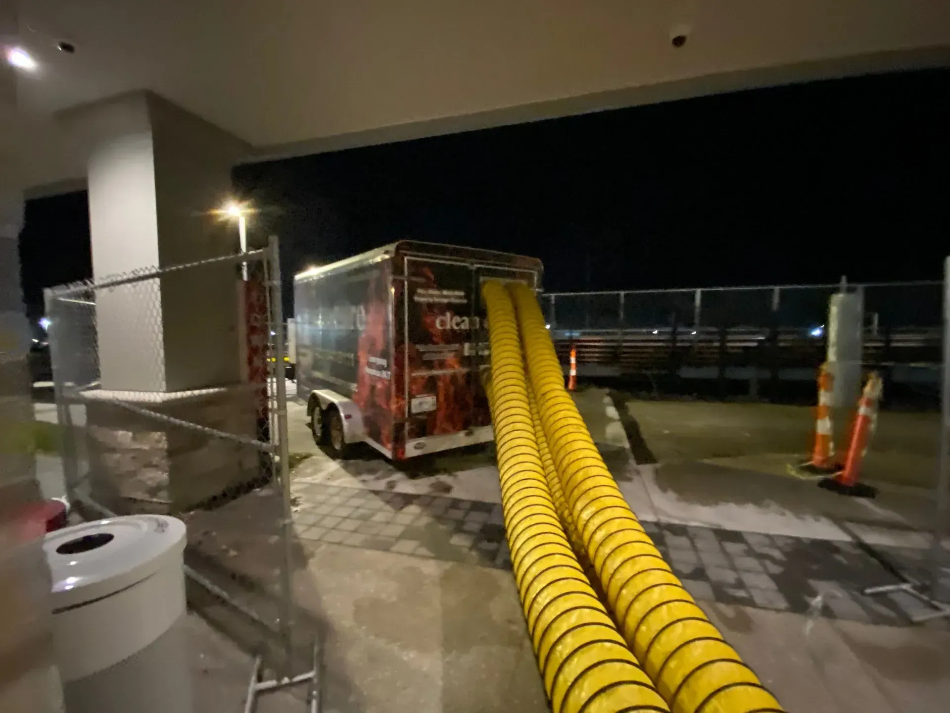 A trailer with two yellow hoses extending. Dark setting.