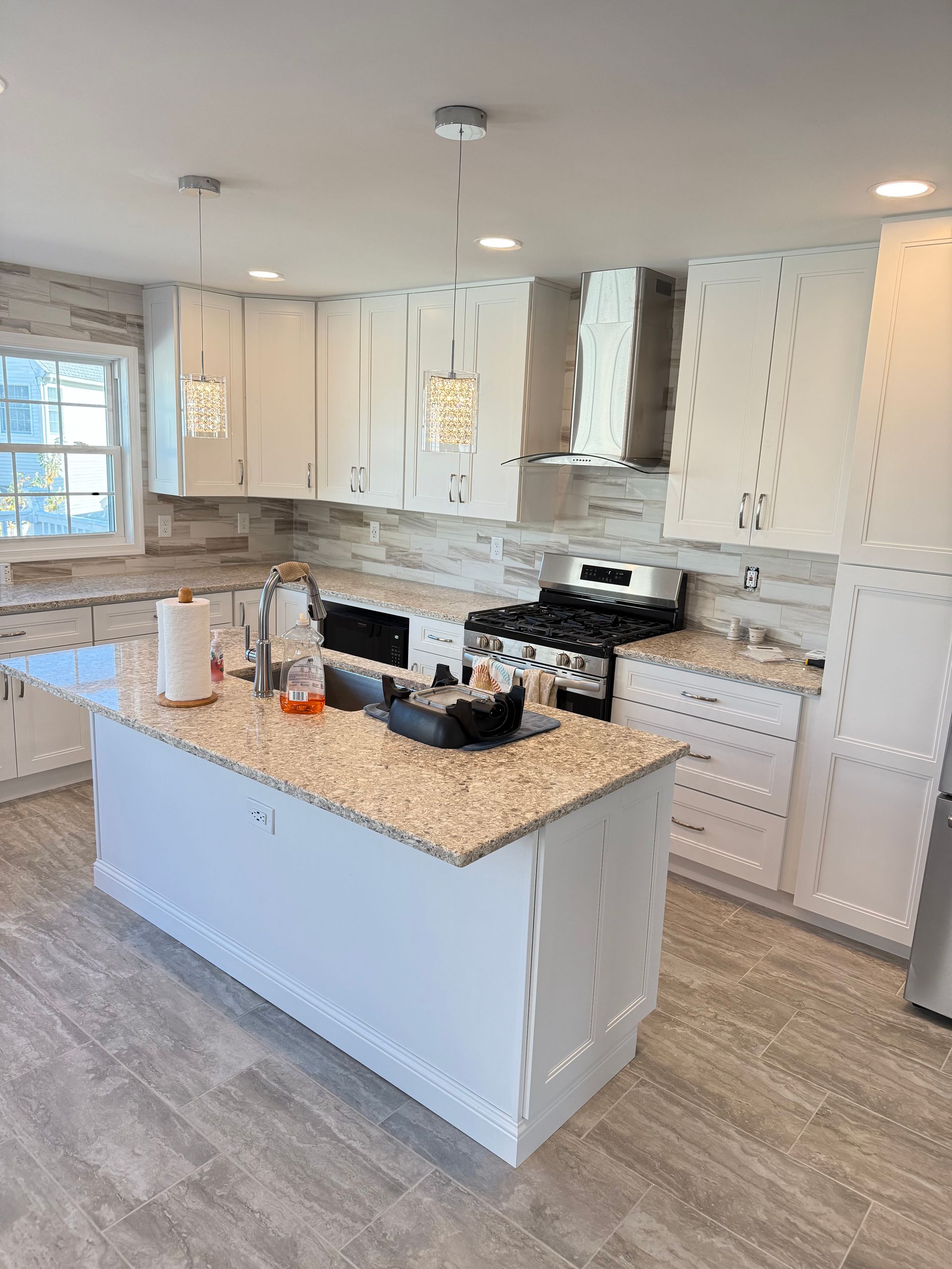 Modern white kitchen with island, range, and stone-look backsplash.