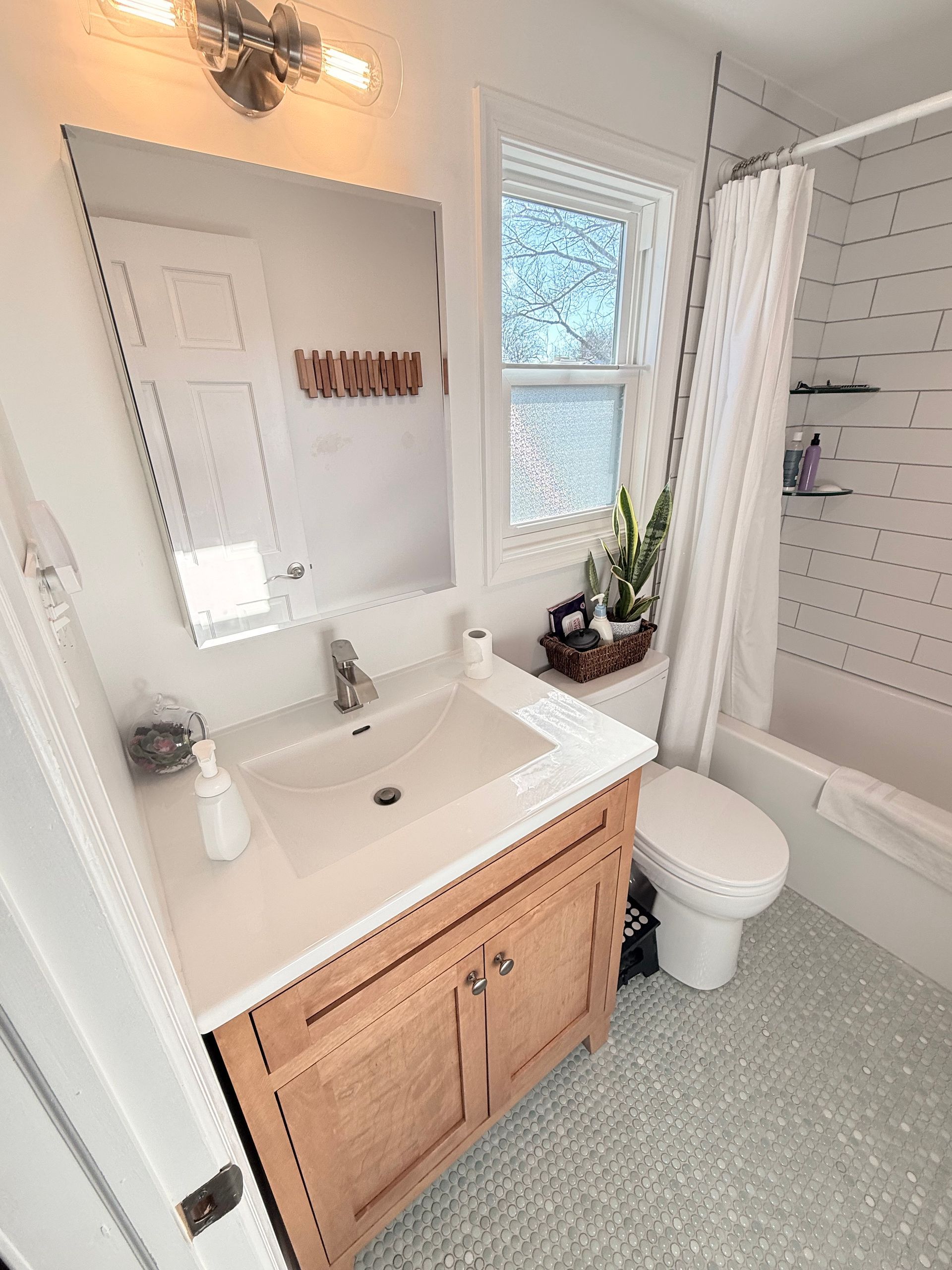 Bathroom with white walls, wood vanity, small window, and mosaic floor tile.