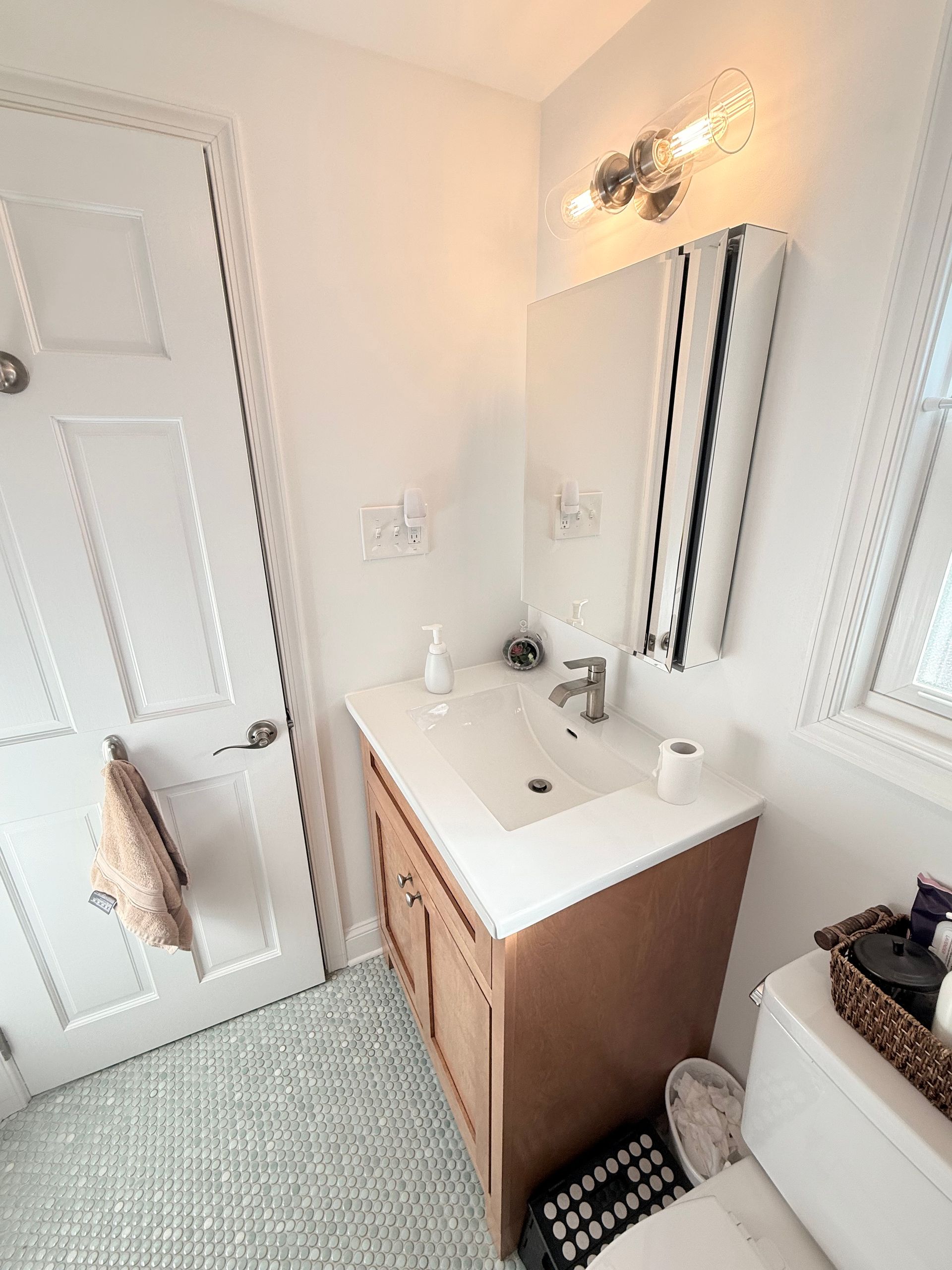 Small bathroom with a white sink vanity, mirror, and light fixture. White door and toilet visible.