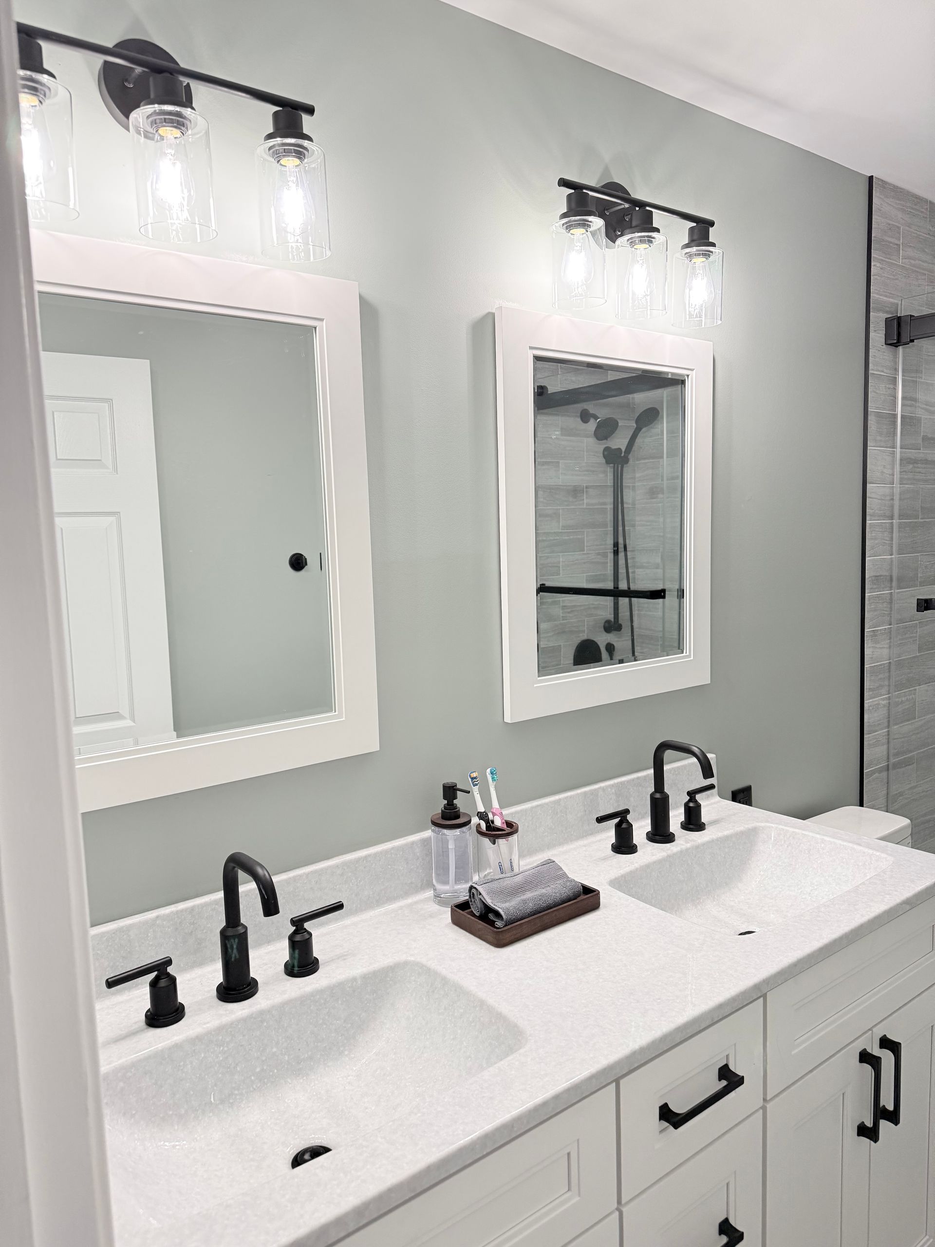 Bathroom with white double vanity, black fixtures, and two matching mirrors with light fixtures above.