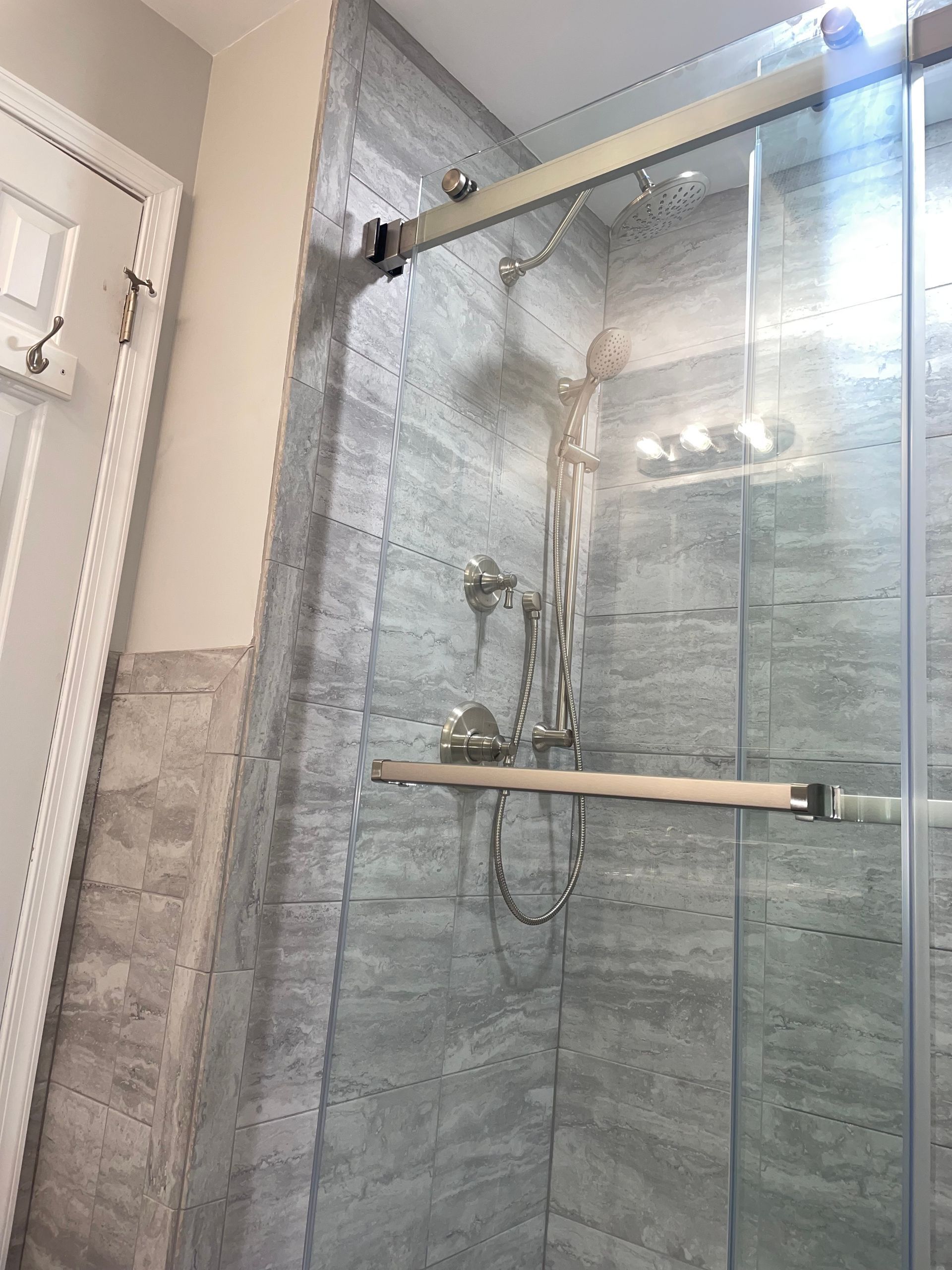 Shower with sliding glass doors, gray tiled walls, and silver shower fixtures.