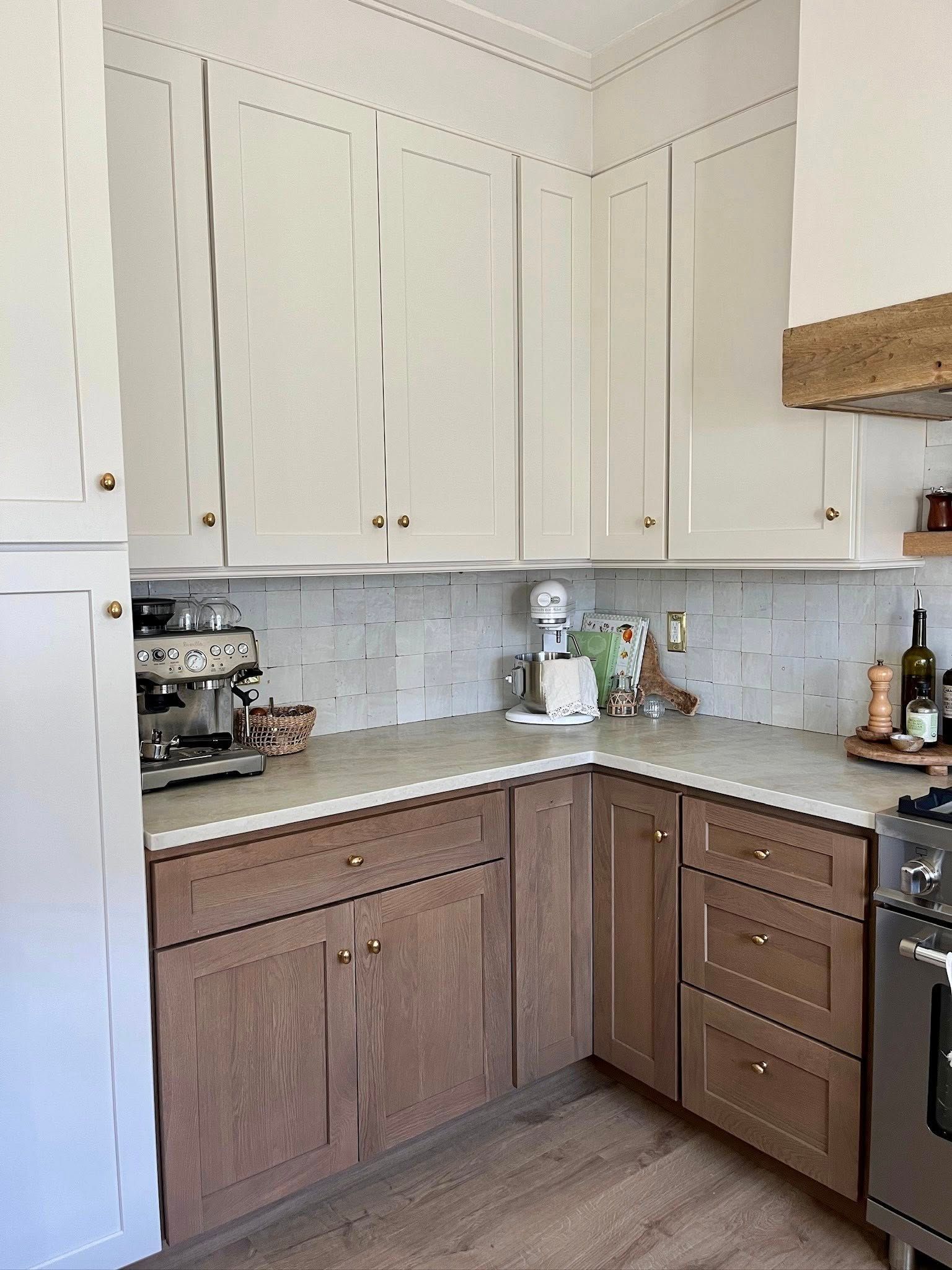 Two-tone kitchen cabinets with light and dark wood, corner layout with appliances and decor.