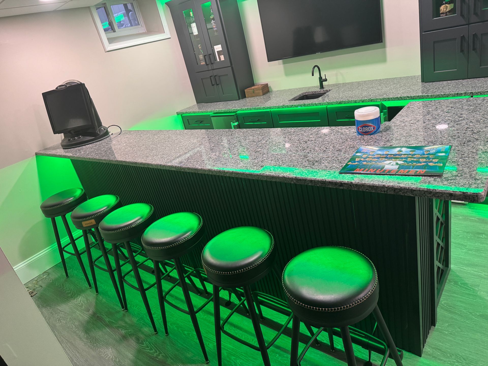 Bar with granite countertop, green LED lighting, six green stools, and black cabinets.