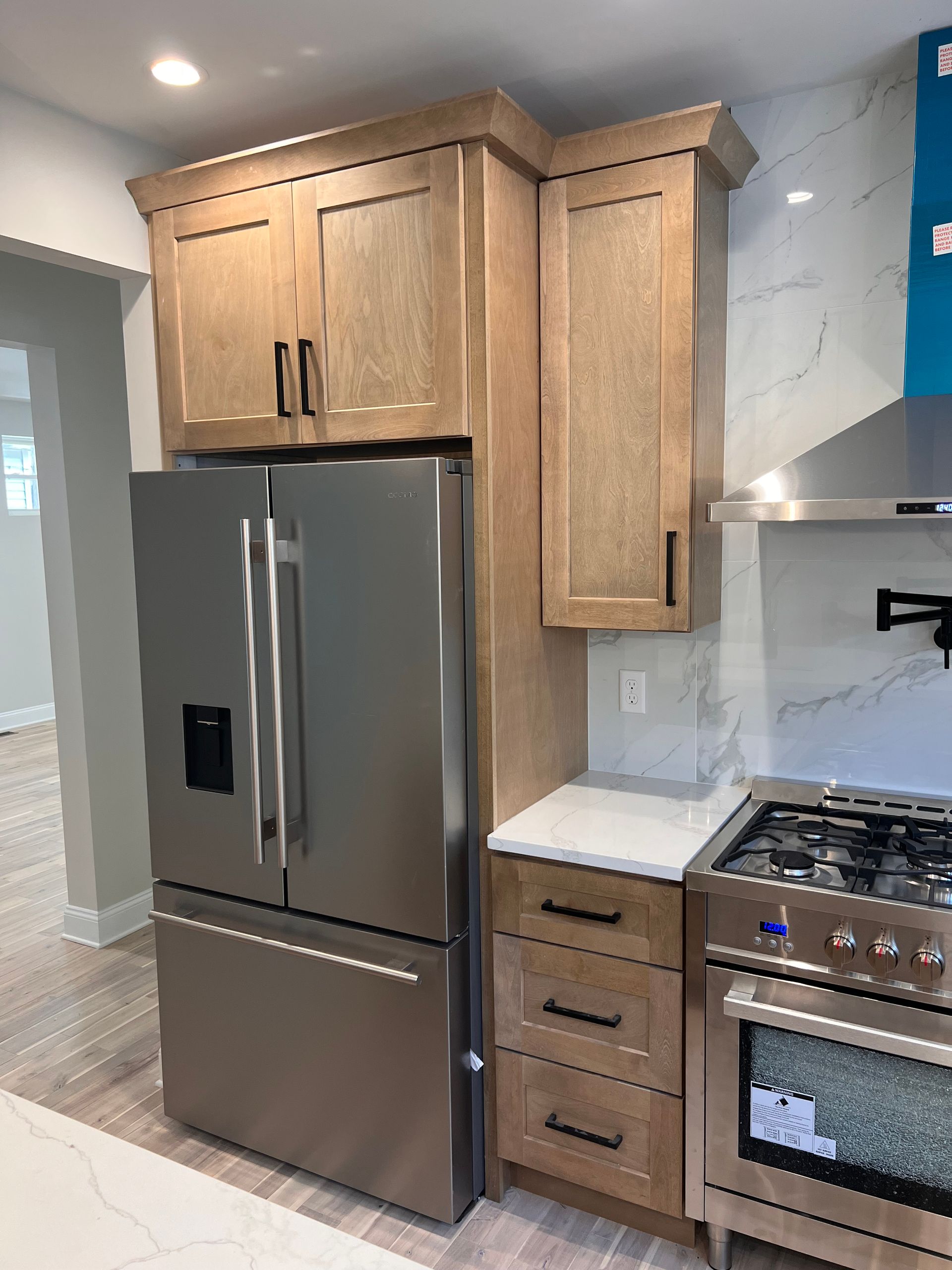 Kitchen with stainless steel refrigerator and light wood cabinets, gas range, and marble backsplash.