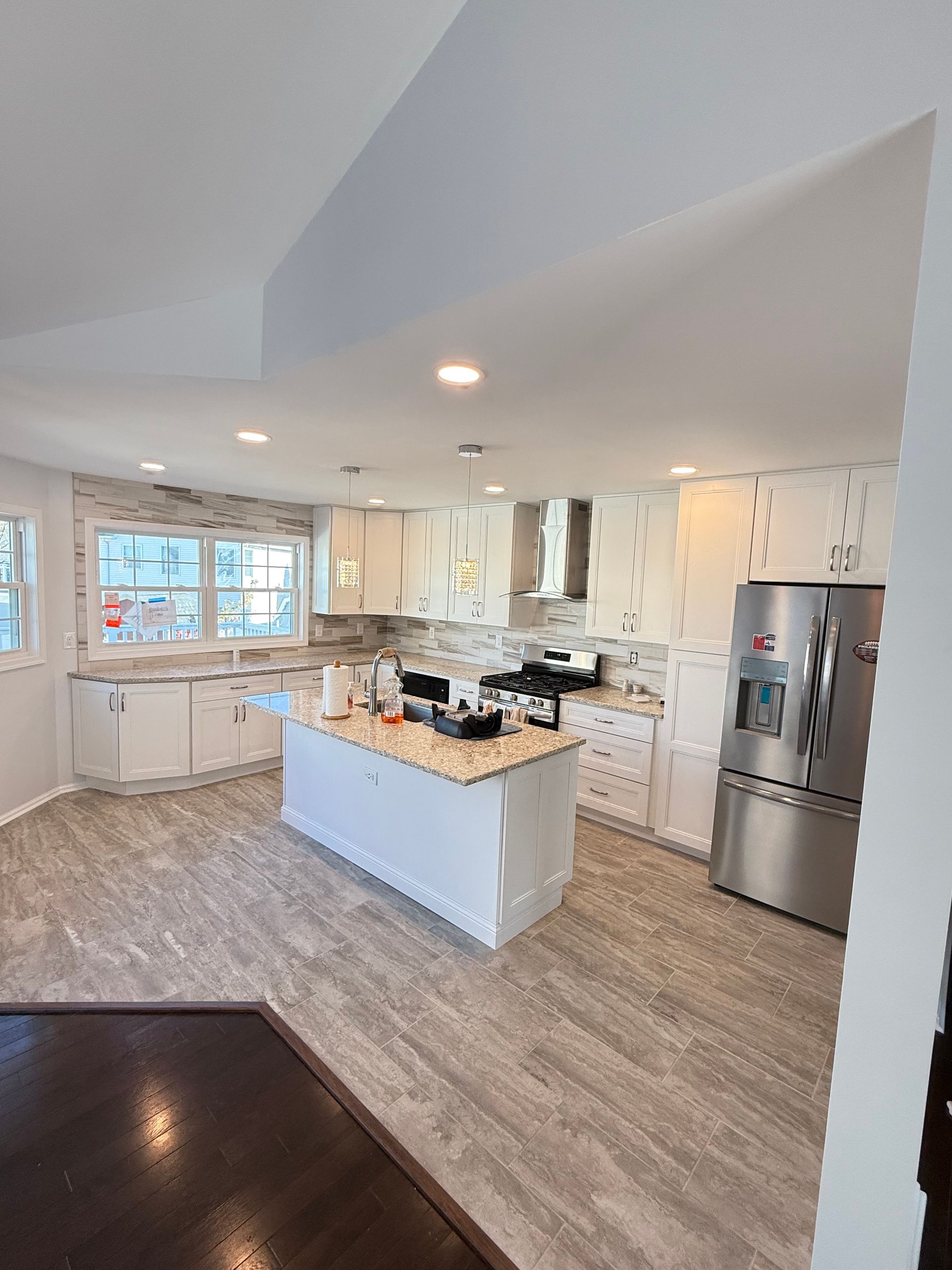 Modern white kitchen with island, stainless steel appliances, and gray wood-look flooring.