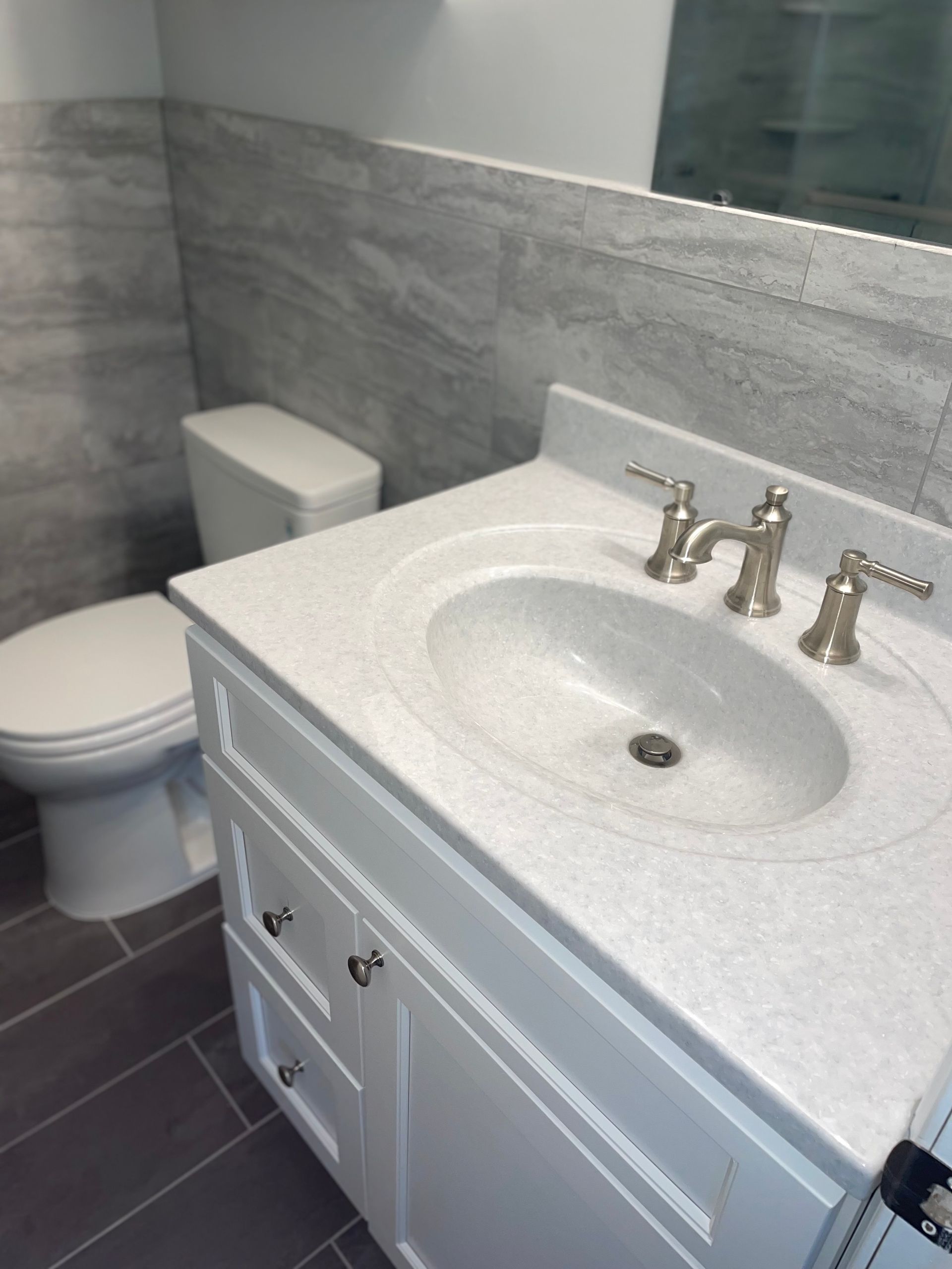 Bathroom vanity with oval sink, white cabinet, gray countertop, and silver faucet fixtures.