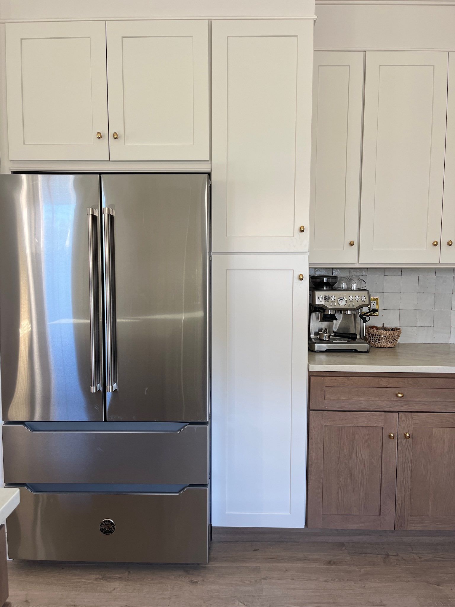 Stainless steel refrigerator and white and brown cabinets in a kitchen setting.