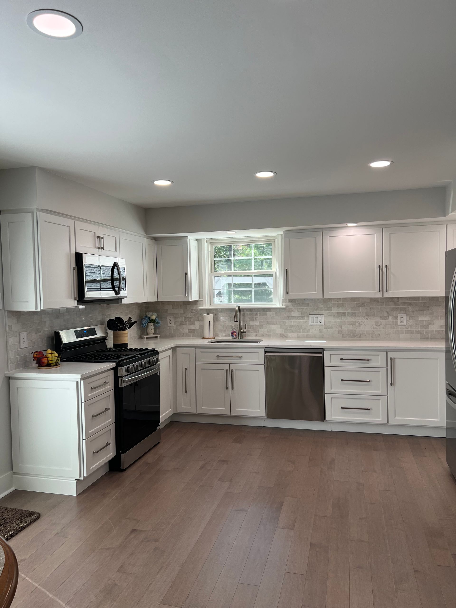 White kitchen with light wood floors, white cabinets, stainless steel appliances, and a window.