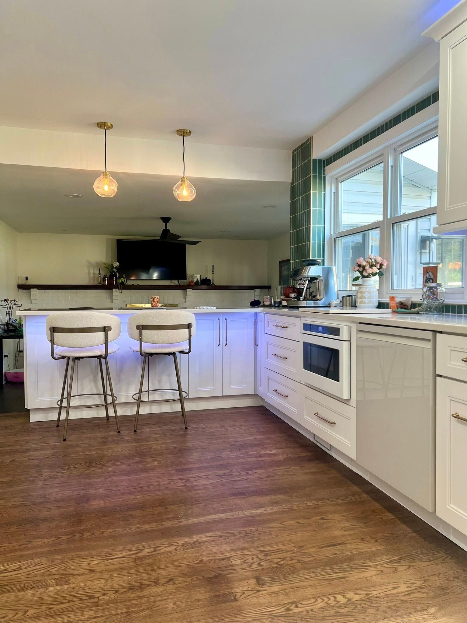 A white kitchen with a peninsula and two bar stools. Golden light fixtures hang above. Cork flooring.