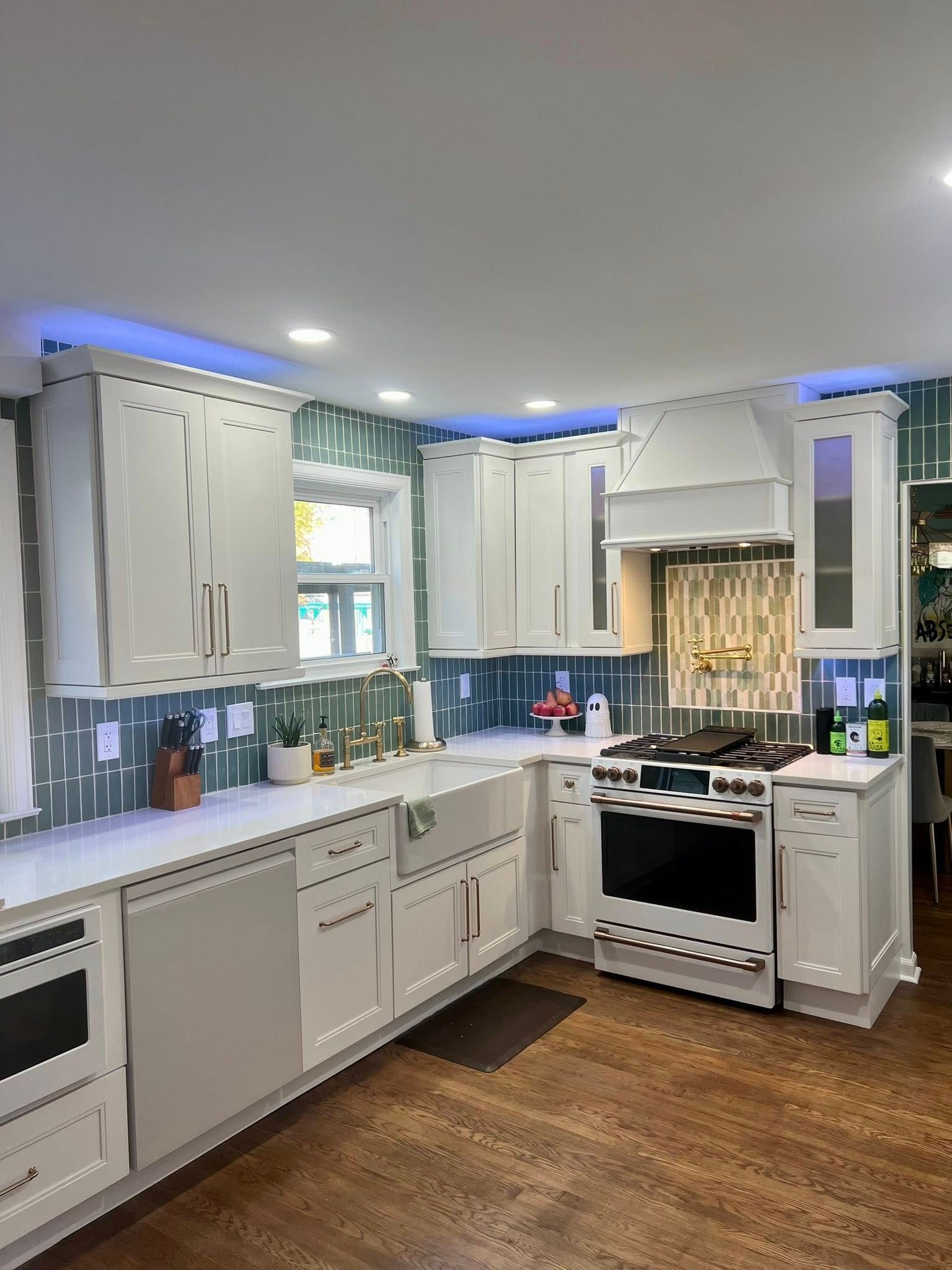 White kitchen with cabinets, stove, sink, and backsplash with blue accent lighting.