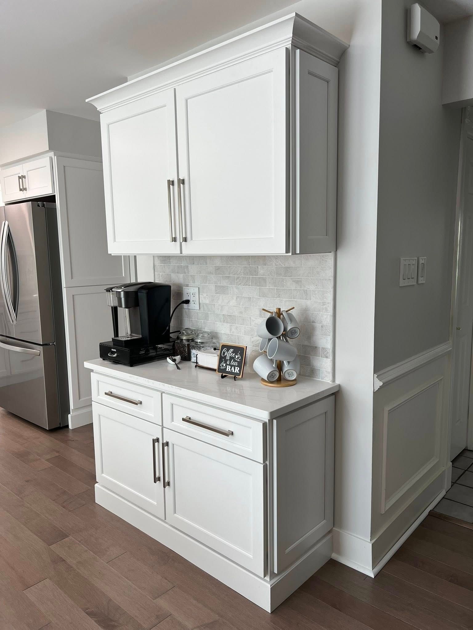 White coffee station with upper and lower cabinets, coffee maker, toaster, and decorative items.