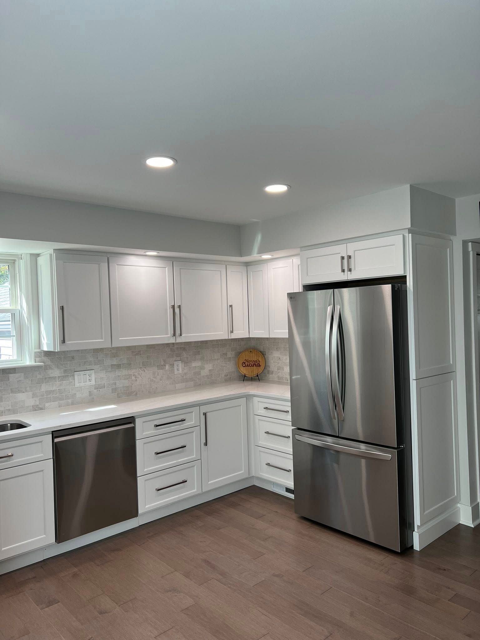 White kitchen with stainless steel appliances, white cabinets, and dark wood floors.