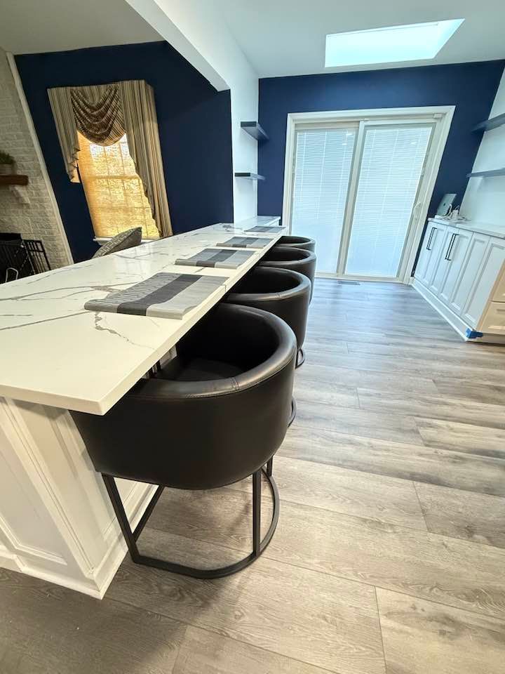 Modern kitchen with a white countertop and black bar stools. Blue wall and sliding door visible.
