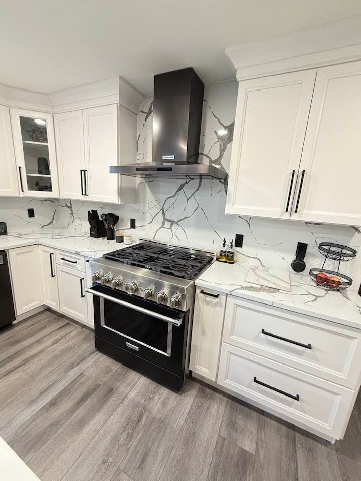 White kitchen with marble backsplash, black oven, and vent hood.