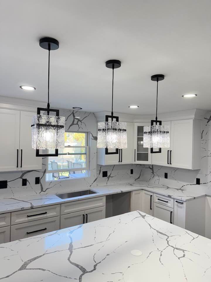Modern kitchen with white cabinets, marble countertops, and three black pendant lights.