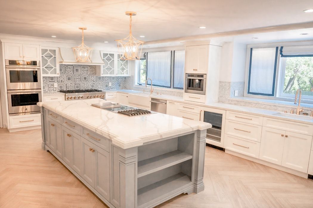 Elegant white kitchen with large island, marble countertops, and patterned backsplash.
