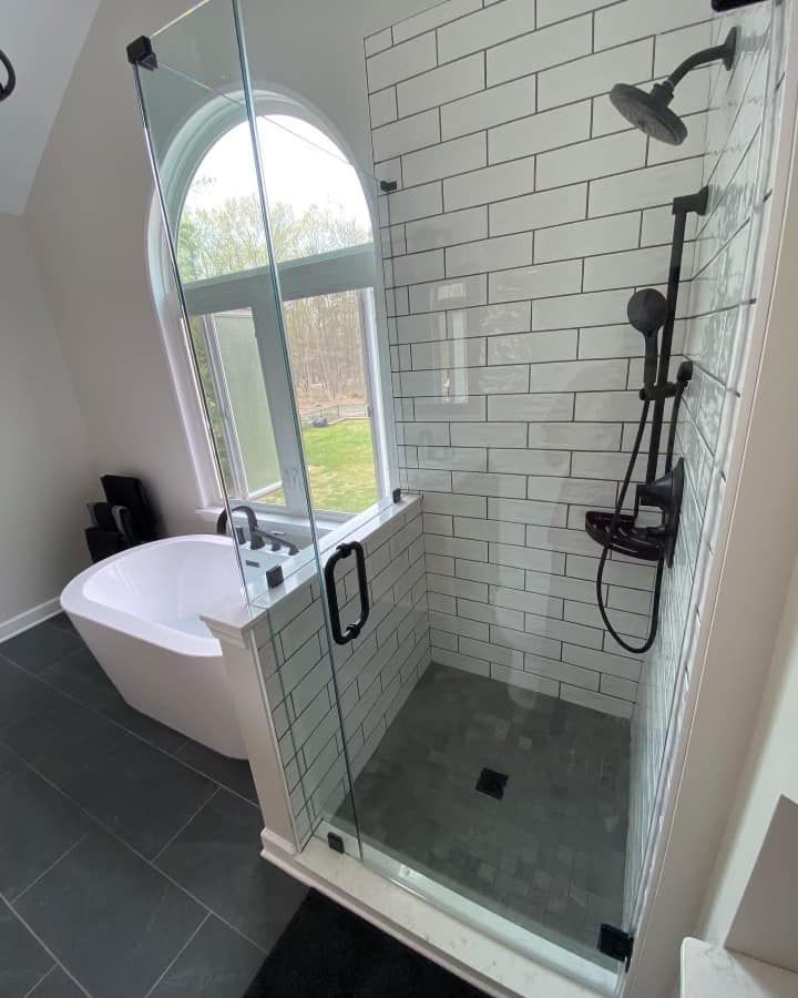 Modern bathroom with a walk-in shower, freestanding tub, arched window, subway tile, and dark fixtures.