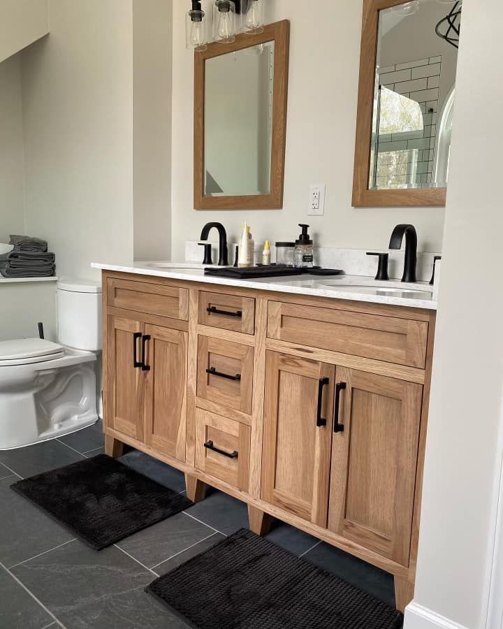Bathroom with a light wood double vanity, black fixtures, mirrors, and dark gray floor tiles.