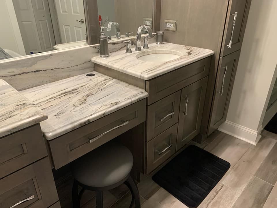 Bathroom vanity with granite countertop, cabinet, mirror, and stool; gray and white color scheme.