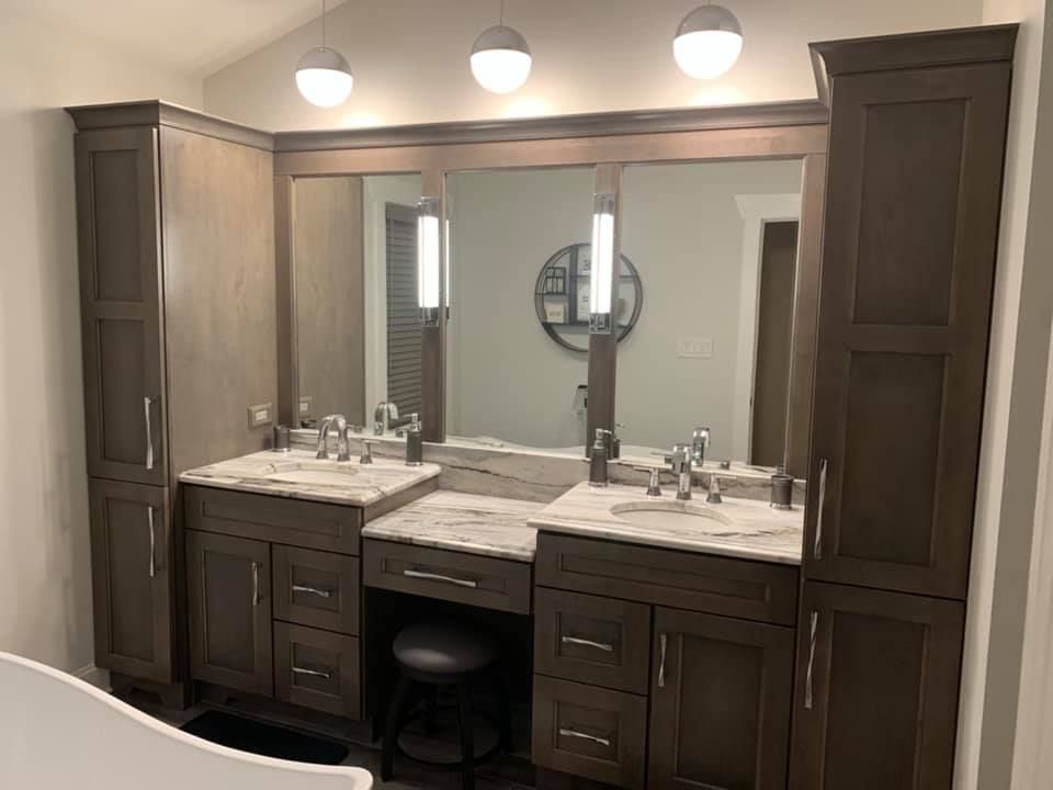 Bathroom vanity with dark cabinets, marble countertops, and large mirror. Three round lights above.