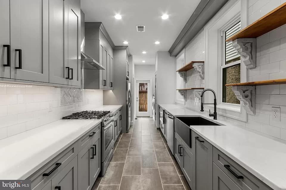Modern, narrow kitchen with gray cabinets, white countertops, and stainless steel appliances.