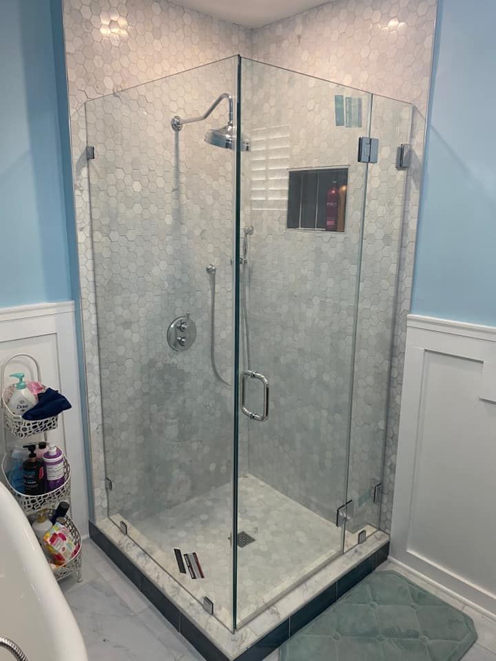 Glass-enclosed corner shower with grey tiled walls, silver fixtures, and a dark tile base. Light blue walls and white trim.