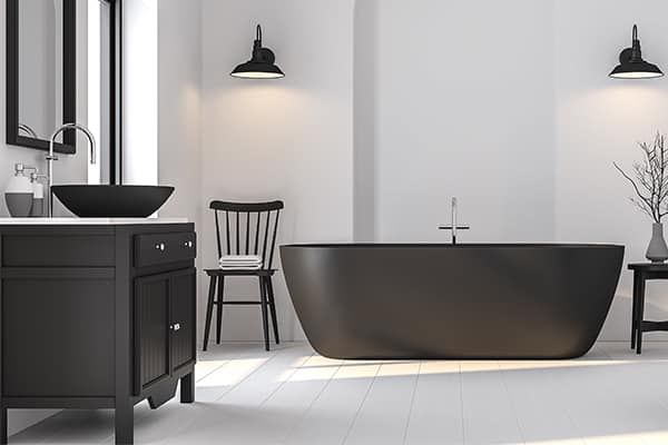 Black and white bathroom with a black bathtub, sink, and cabinet. Two wall sconces illuminate the space.