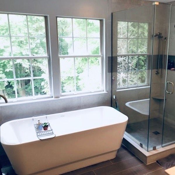 Bathroom with freestanding tub, glass shower, and windows overlooking greenery. Beige walls, wood-look floor.