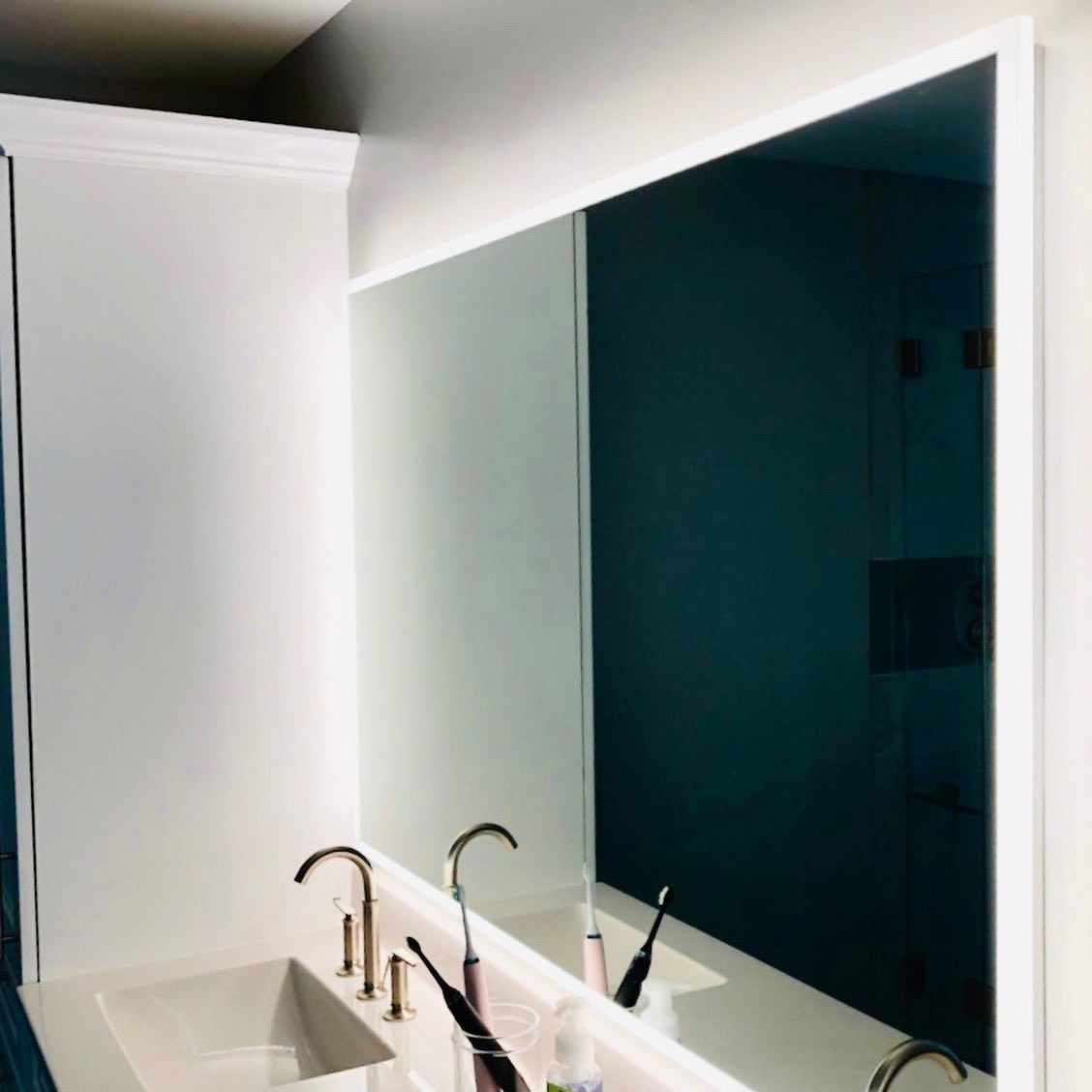 Large bathroom mirror with backlighting above a sink and faucet.