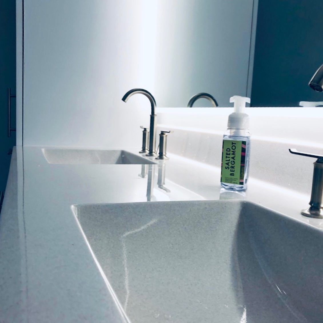 White bathroom sinks with chrome faucets, hand soap bottle, and mirror.