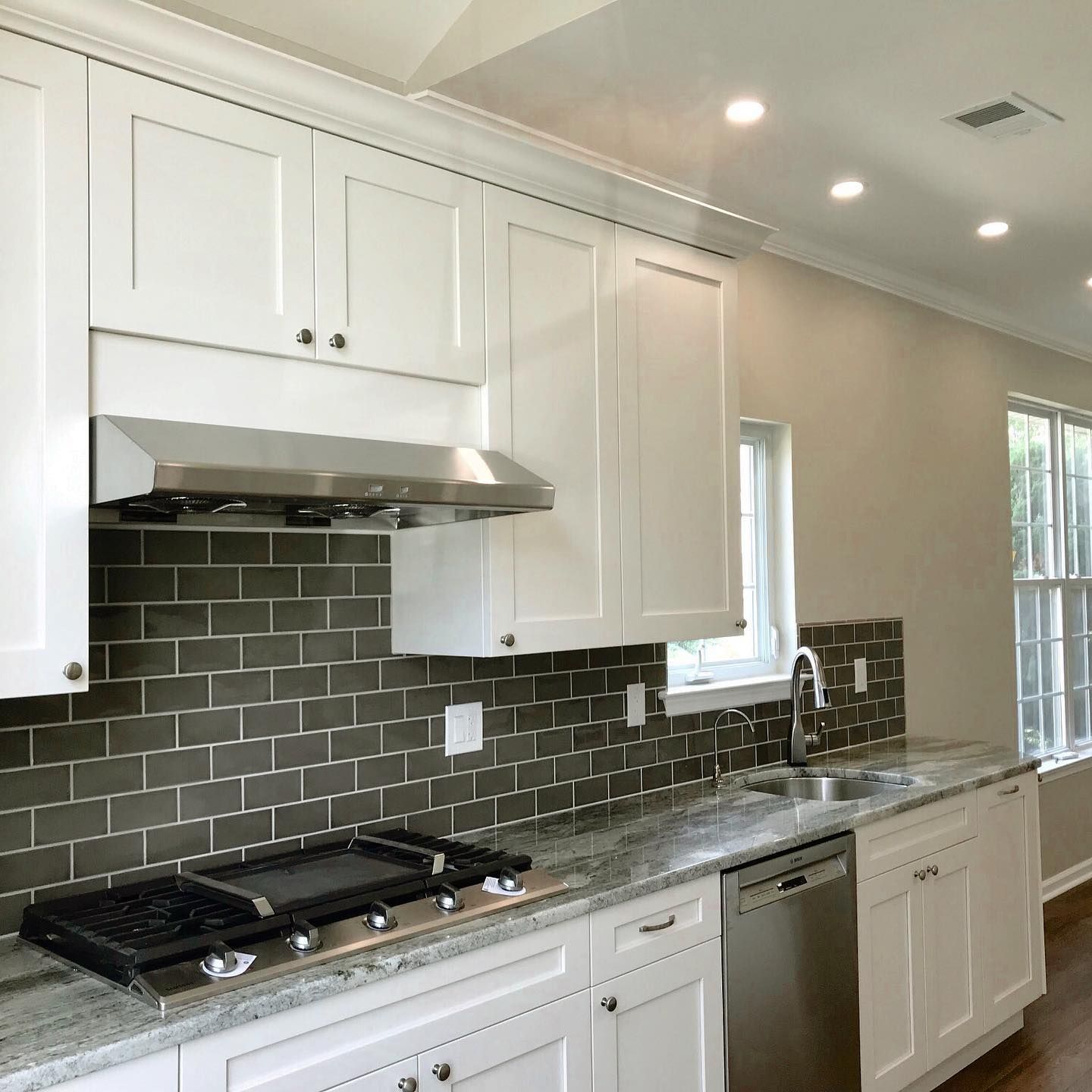 White kitchen with gray tile backsplash, stainless steel appliances, and granite countertops.