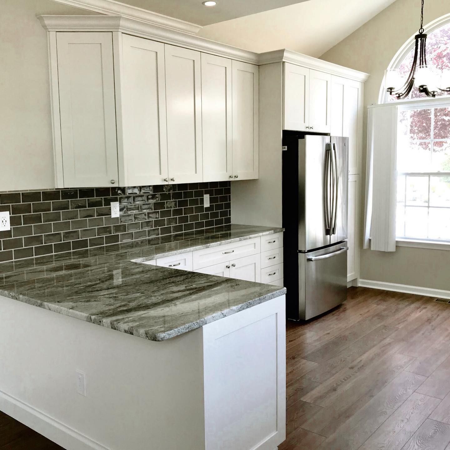 White kitchen with granite countertops, stainless steel appliances, and dark tile backsplash.
