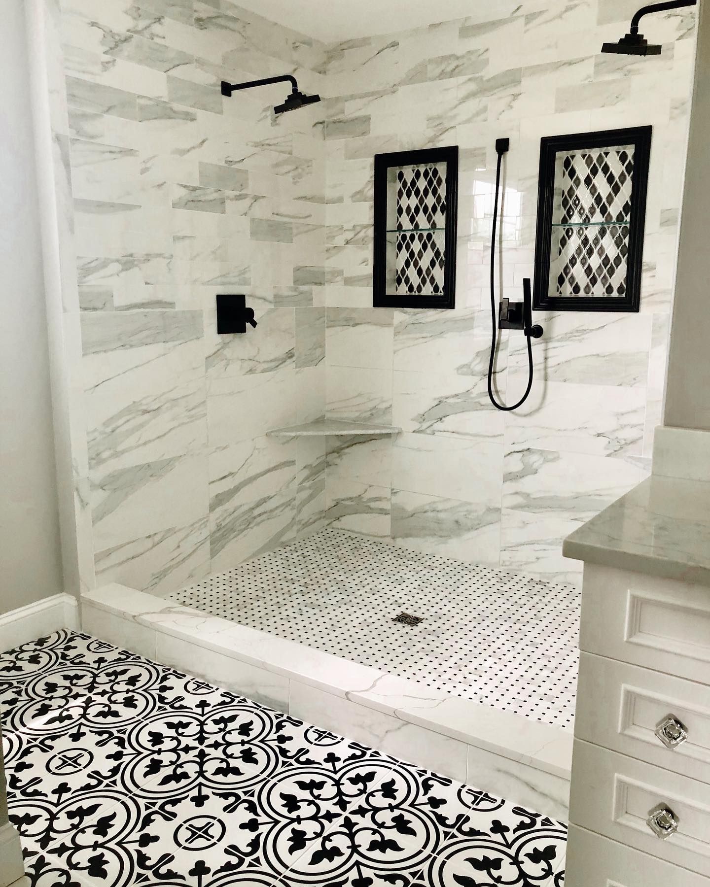 Bathroom with marble shower walls, black and white patterned floor tiles, and black fixtures.