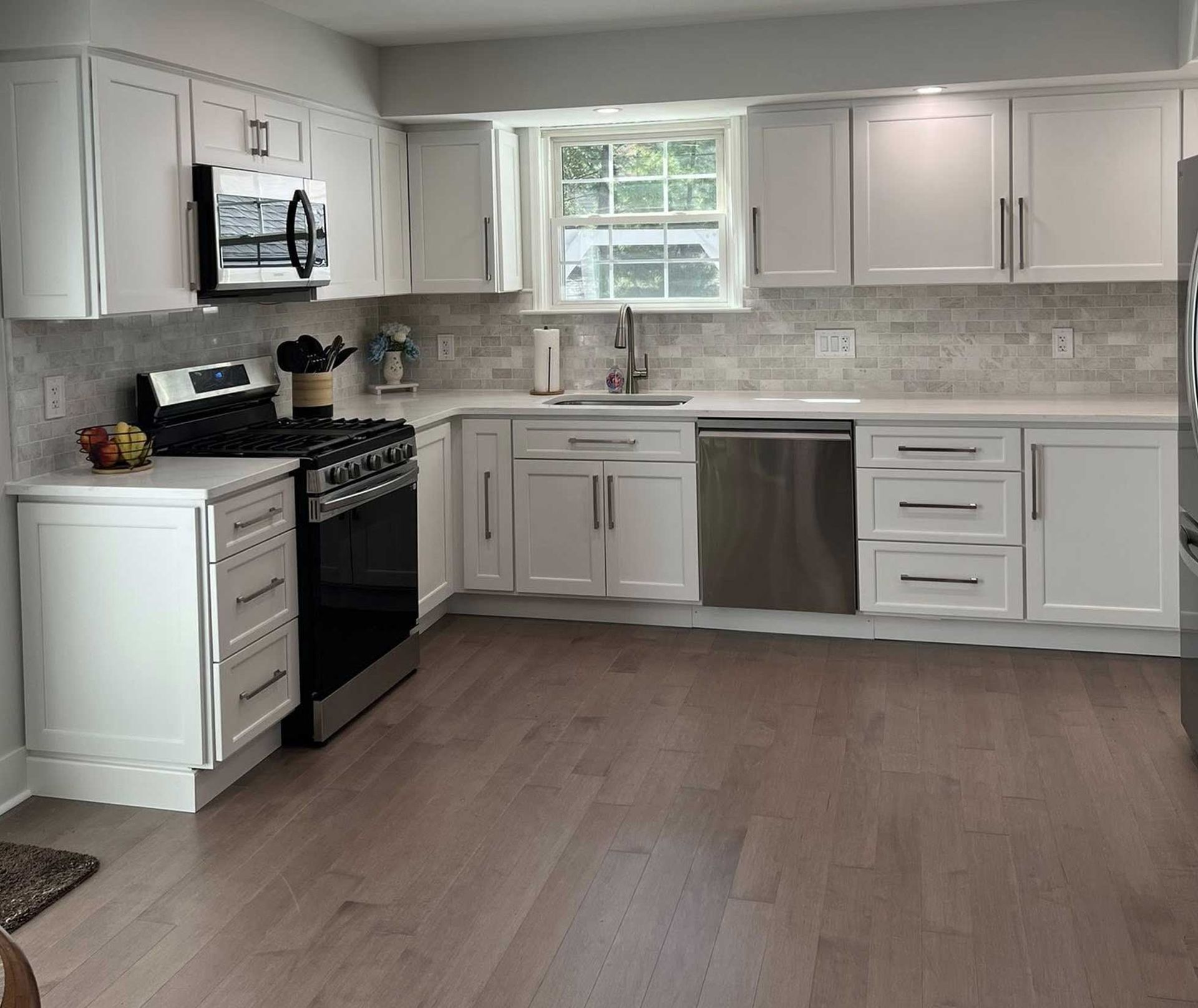 White kitchen with white cabinets, stainless steel appliances, and light wood flooring.