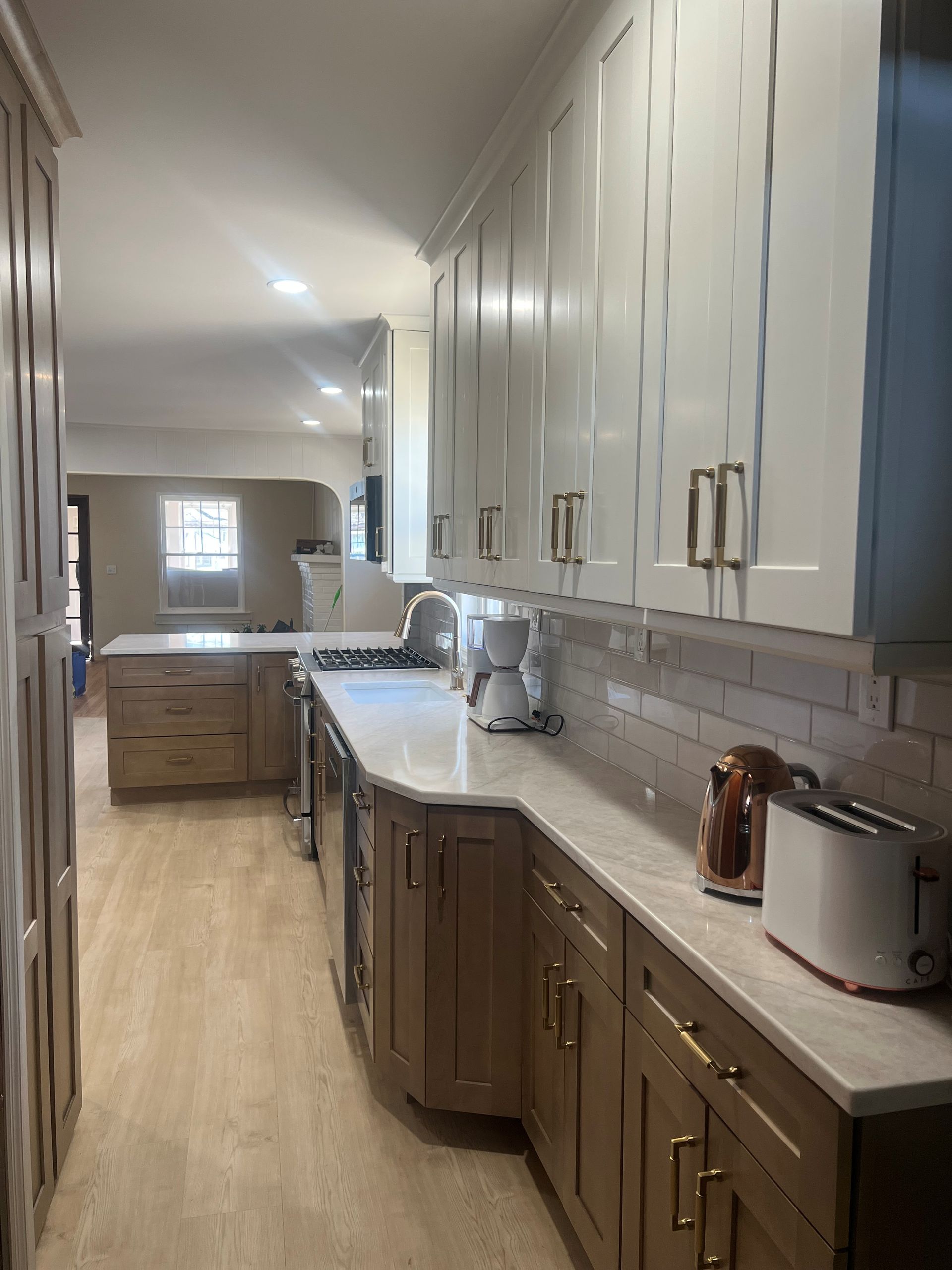 A bright kitchen features white upper cabinets, wood lower cabinets, light countertops, and a subway tile backsplash. 